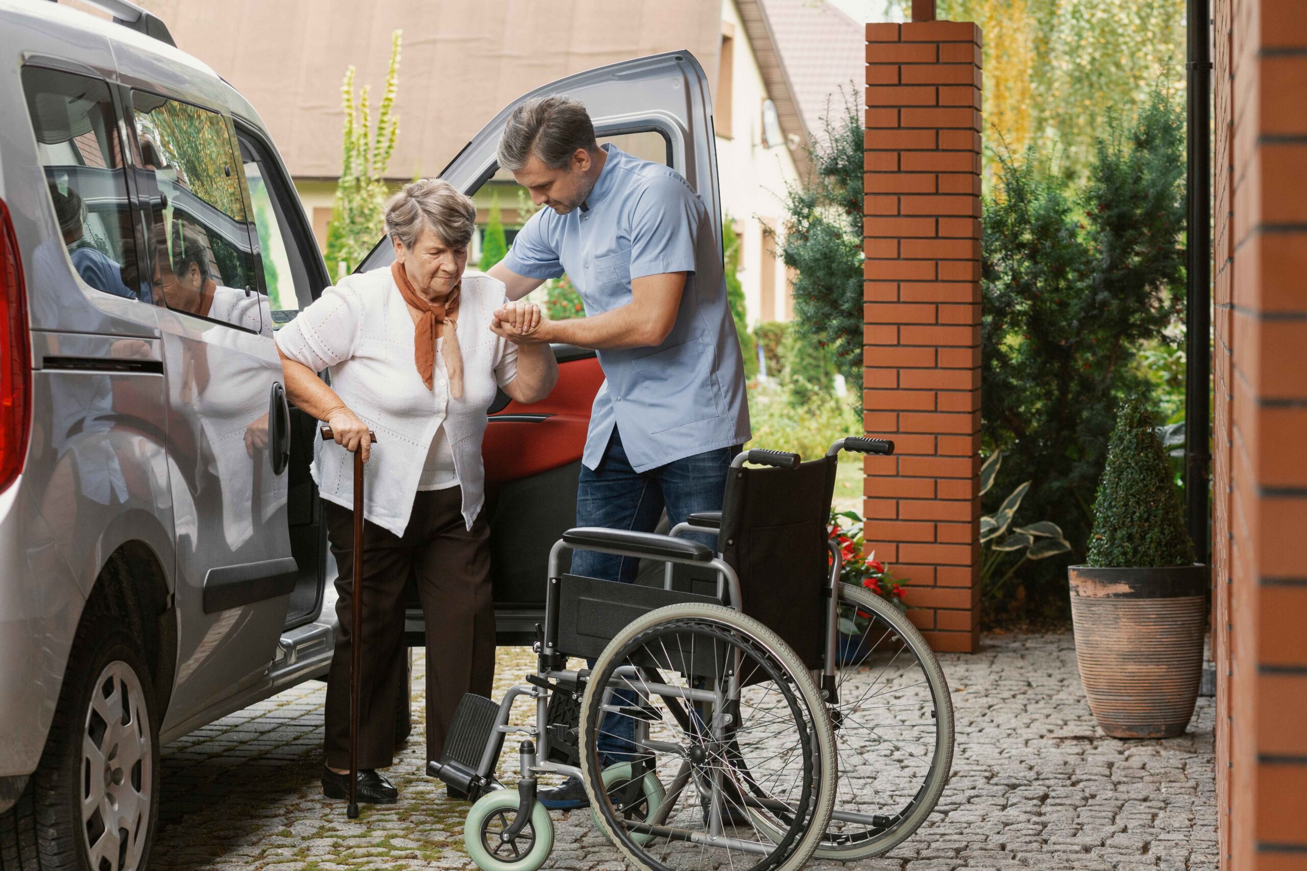 Senior woman receiving caregiver assistance while getting out of a car.